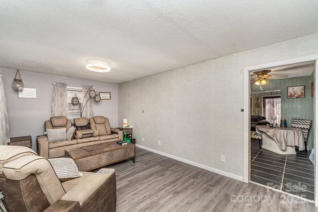 living room featuring ceiling fan, a textured ceiling, baseboards, and wood finished floors