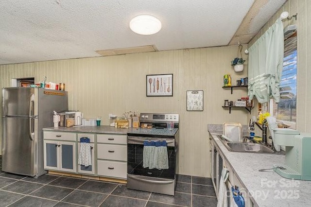 kitchen with a textured ceiling, stainless steel appliances, dark tile patterned floors, a sink, and light countertops