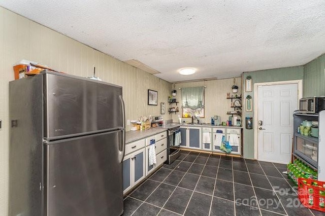 kitchen featuring a textured ceiling, dark tile patterned flooring, and appliances with stainless steel finishes