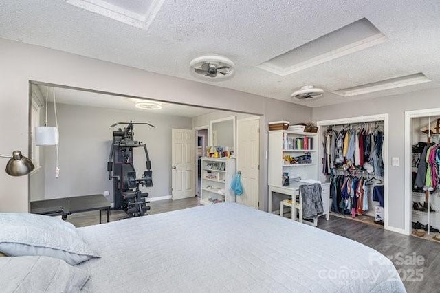 bedroom featuring a textured ceiling, baseboards, wood finished floors, and multiple closets