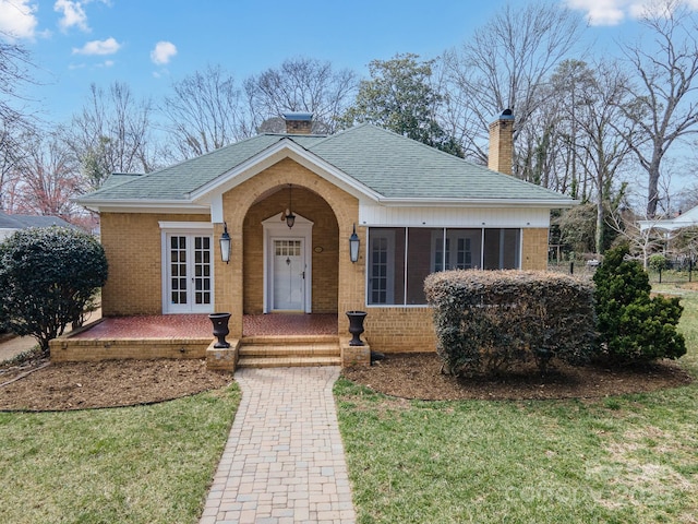 view of front of house featuring roof with shingles, brick siding, a chimney, and a front lawn