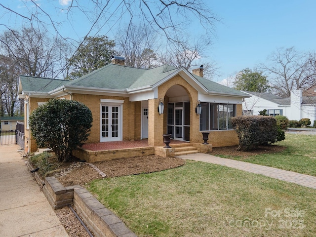 bungalow-style home with french doors, brick siding, a front lawn, and roof with shingles