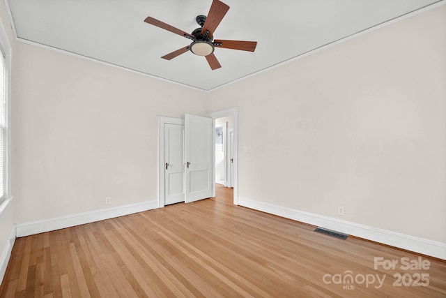 spare room with ceiling fan, wood finished floors, visible vents, baseboards, and crown molding