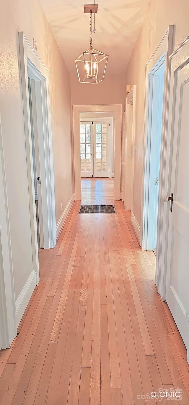 corridor featuring french doors, a notable chandelier, light wood-style flooring, and baseboards
