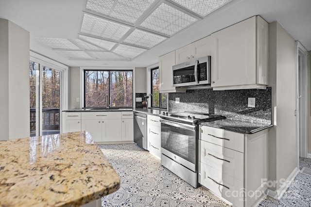 kitchen featuring backsplash, appliances with stainless steel finishes, white cabinetry, a sink, and dark stone countertops