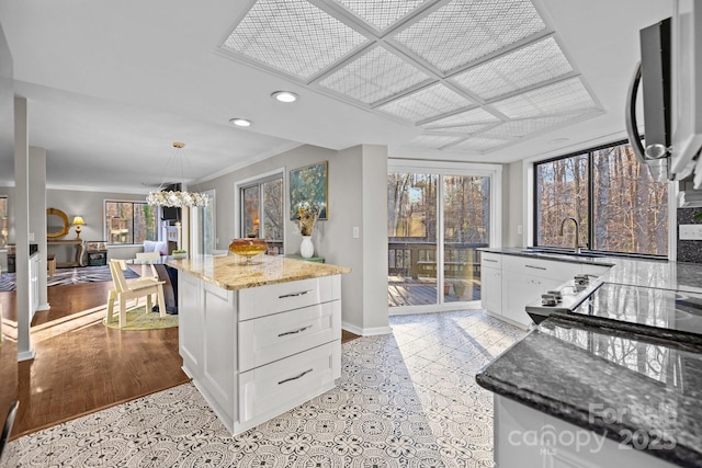 kitchen with a kitchen island, a sink, white cabinets, light stone countertops, and pendant lighting