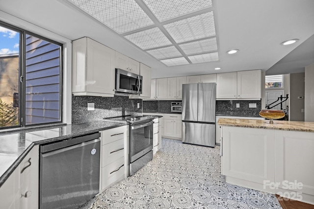 kitchen featuring plenty of natural light, stainless steel appliances, dark stone countertops, and white cabinetry