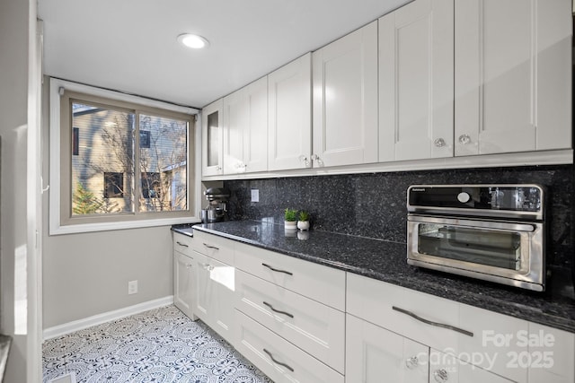 kitchen featuring light tile patterned floors, tasteful backsplash, white cabinetry, dark stone counters, and baseboards