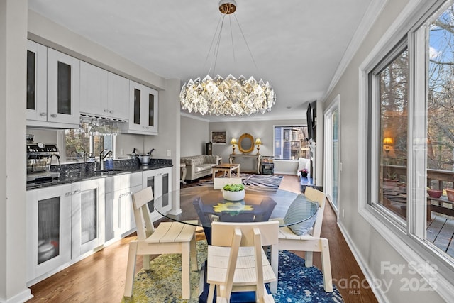 dining space with beverage cooler, baseboards, ornamental molding, wood finished floors, and a chandelier