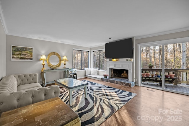 living room featuring a fireplace with raised hearth, wood finished floors, visible vents, and crown molding