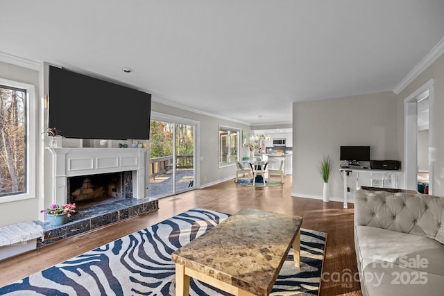 living area with baseboards, ornamental molding, a fireplace with raised hearth, and wood finished floors