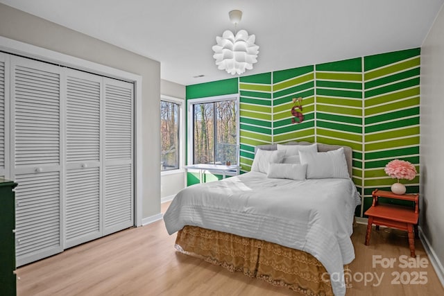 bedroom featuring an accent wall, a closet, wood finished floors, and baseboards