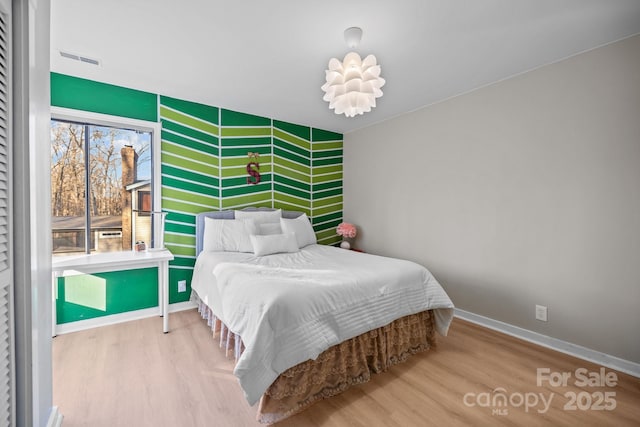 bedroom with an accent wall, wood finished floors, visible vents, and baseboards