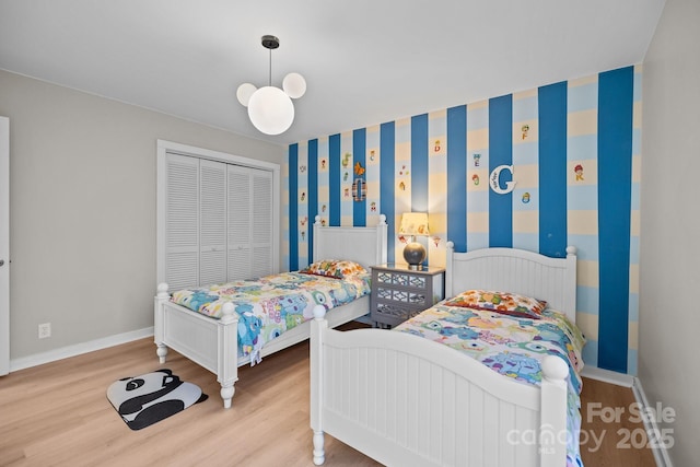 bedroom with wallpapered walls, light wood-style flooring, baseboards, and a closet