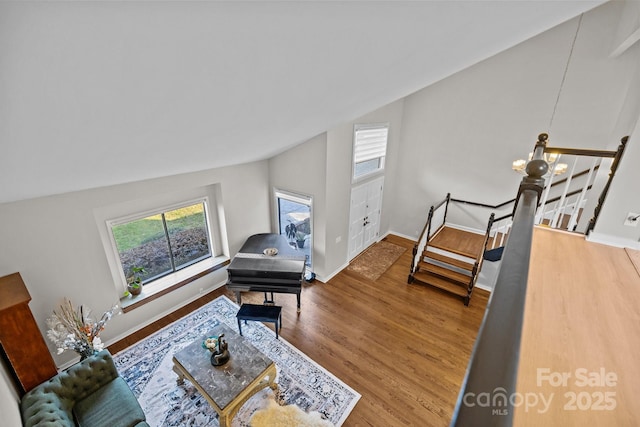 living room featuring lofted ceiling, wood finished floors, baseboards, and an inviting chandelier