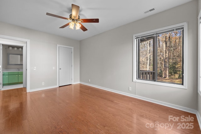 unfurnished bedroom with visible vents, a ceiling fan, connected bathroom, wood finished floors, and baseboards