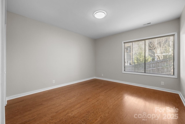 spare room featuring wood finished floors, visible vents, and baseboards