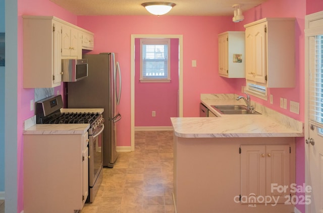 kitchen featuring a sink, appliances with stainless steel finishes, a peninsula, light countertops, and baseboards