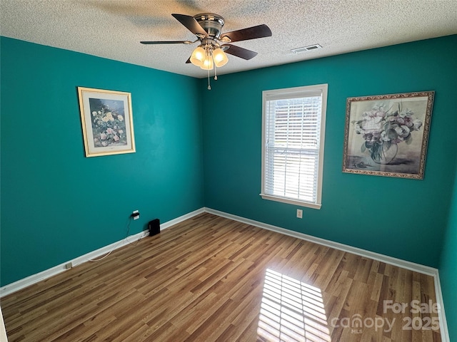 spare room with visible vents, ceiling fan, baseboards, wood finished floors, and a textured ceiling