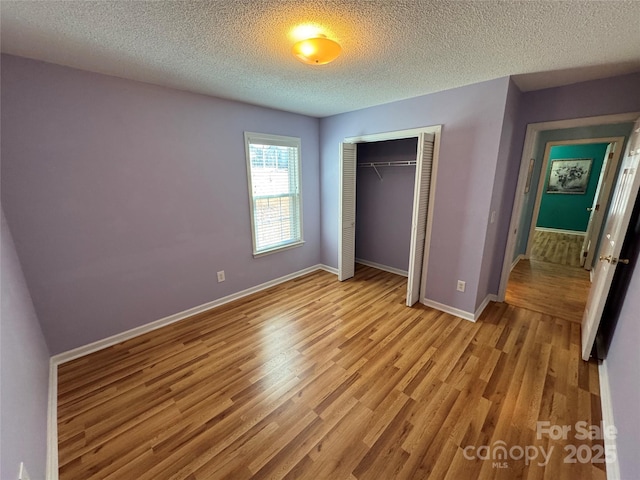 unfurnished bedroom featuring baseboards, a closet, light wood finished floors, and a textured ceiling