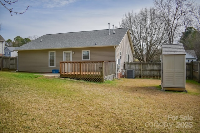 rear view of property with cooling unit, a fenced backyard, an outdoor structure, a deck, and a lawn