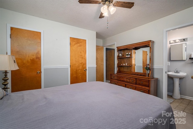 bedroom with a sink, ceiling fan, a textured ceiling, and ensuite bath