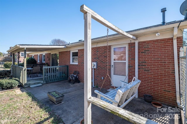 rear view of house with covered porch, a patio, and brick siding