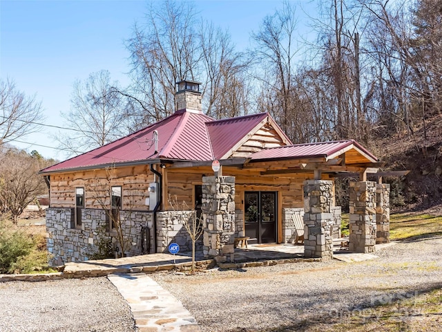 view of front of home with stone siding, metal roof, and a chimney