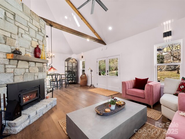 living area featuring light wood finished floors, a ceiling fan, beamed ceiling, a fireplace, and high vaulted ceiling