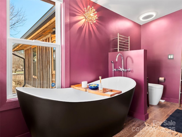 interior space featuring a soaking tub, wood finished floors, and toilet