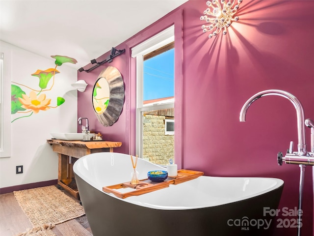 full bath with a sink, a freestanding bath, baseboards, and wood finished floors