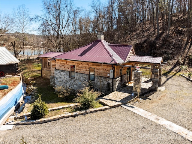 view of property exterior with stone siding, a chimney, and metal roof