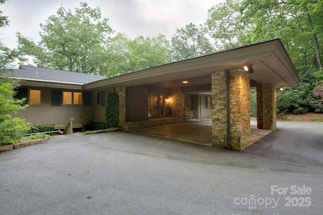 view of front of home featuring a carport, stone siding, driveway, and a shingled roof