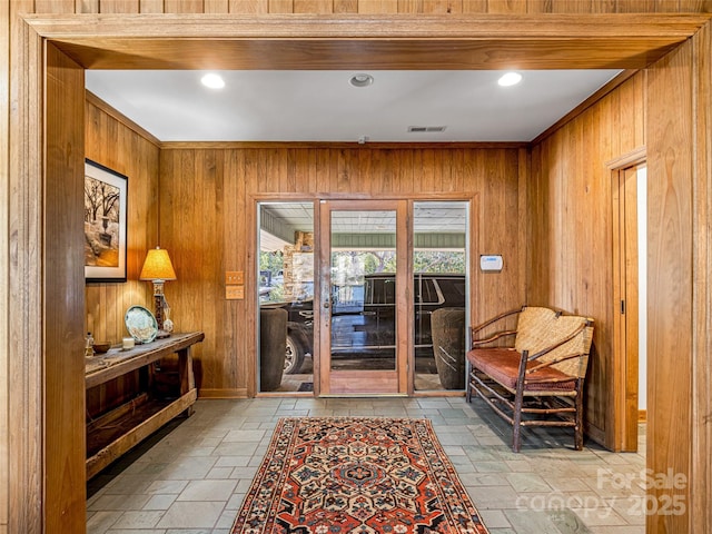 doorway to outside featuring visible vents, wood walls, stone tile flooring, and crown molding