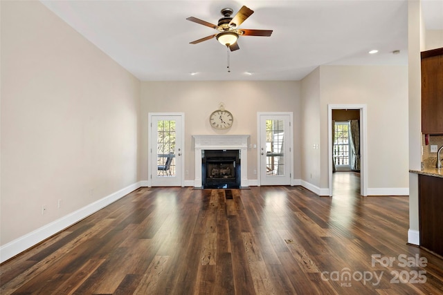 unfurnished living room with ceiling fan, recessed lighting, a fireplace with flush hearth, baseboards, and dark wood-style floors