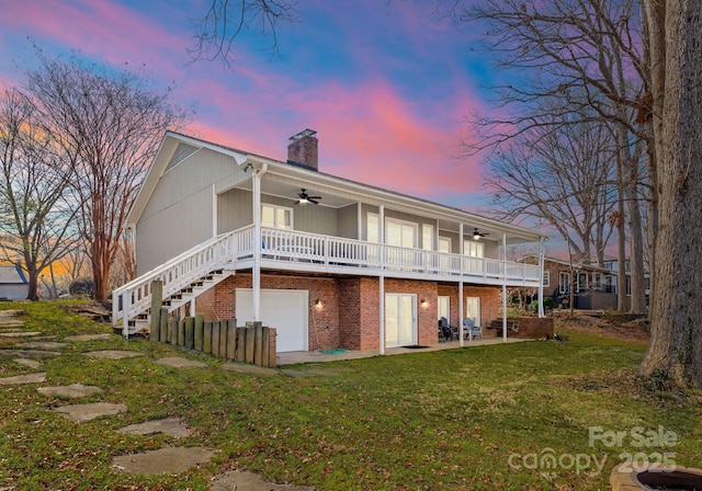 back of property at dusk featuring brick siding, a yard, a chimney, stairway, and a ceiling fan