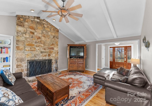 living room featuring baseboards, a stone fireplace, ceiling fan, wood finished floors, and vaulted ceiling with beams