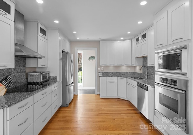 kitchen featuring wall chimney range hood, recessed lighting, a sink, and appliances with stainless steel finishes