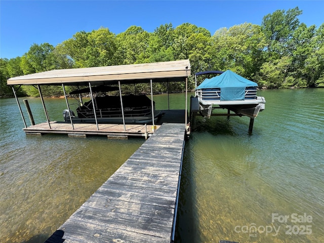 dock area featuring a water view, boat lift, and a wooded view