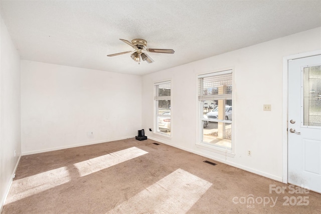 carpeted spare room with a ceiling fan, visible vents, a textured ceiling, and baseboards