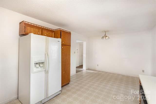 kitchen featuring a textured ceiling, white fridge with ice dispenser, light floors, and brown cabinetry