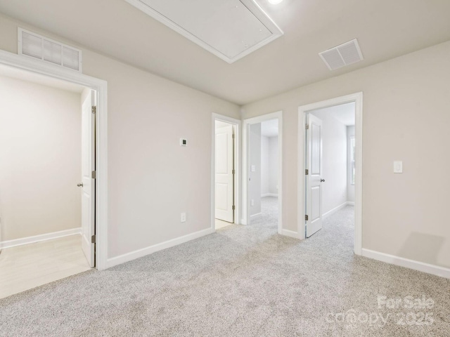 carpeted empty room with attic access, visible vents, and baseboards