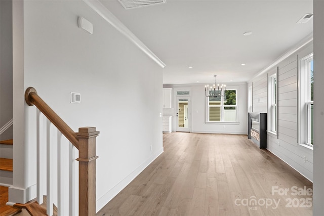 unfurnished living room with crown molding, an inviting chandelier, visible vents, and light wood-style floors