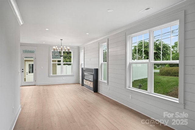 unfurnished living room with recessed lighting, visible vents, light wood-style flooring, a glass covered fireplace, and a chandelier