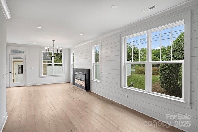 unfurnished living room with light wood finished floors, plenty of natural light, visible vents, a glass covered fireplace, and a chandelier