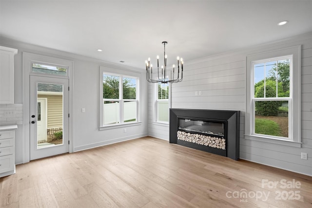 unfurnished living room featuring a notable chandelier, recessed lighting, light wood-style floors, a glass covered fireplace, and ornamental molding