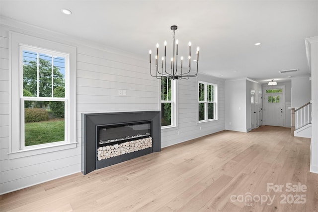 unfurnished living room featuring light wood finished floors, ornamental molding, stairway, and a healthy amount of sunlight