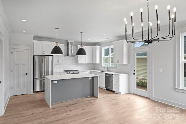 kitchen featuring a center island, stainless steel appliances, light countertops, white cabinetry, and wall chimney range hood