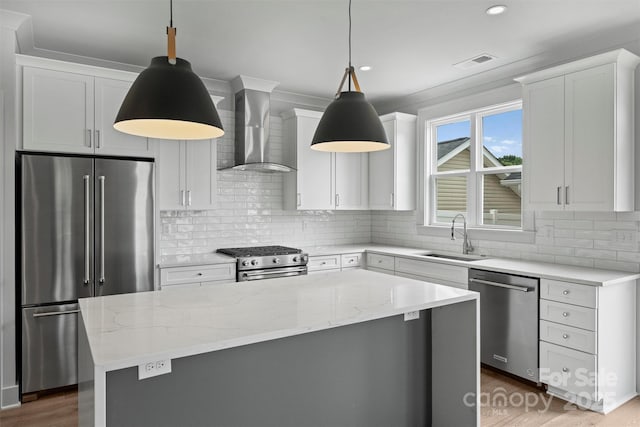 kitchen featuring high quality appliances, decorative light fixtures, a center island, wall chimney range hood, and a sink