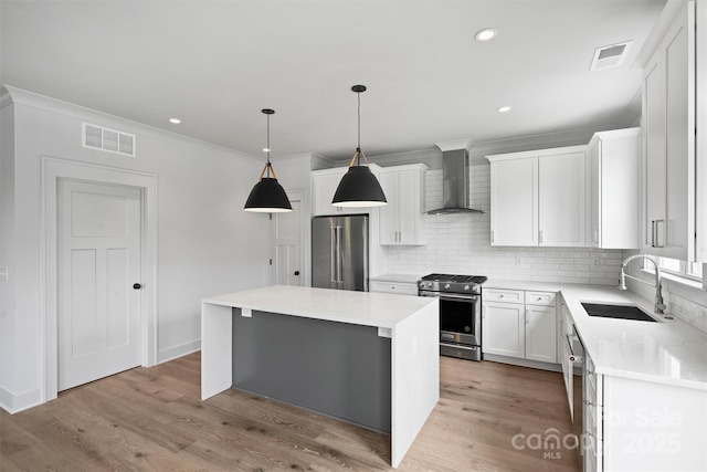 kitchen with a sink, a kitchen island, white cabinetry, appliances with stainless steel finishes, and wall chimney range hood